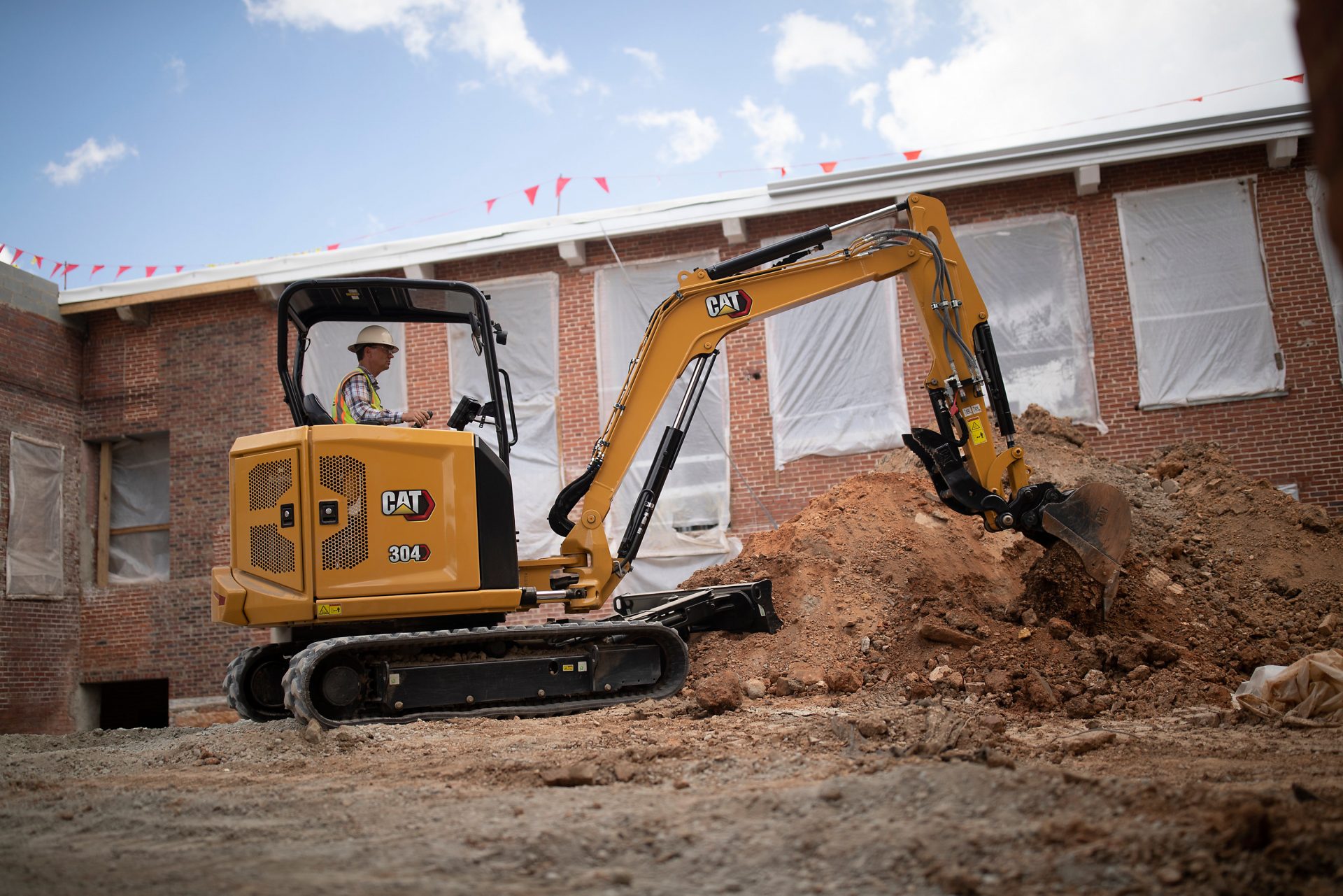 CAT's next-gen 304 mini excavator scooping material on a job site.