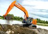 A hitachi excavator moves dirt near a lake