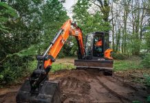 A Develon -7 series mini excavator digs in a forest setting