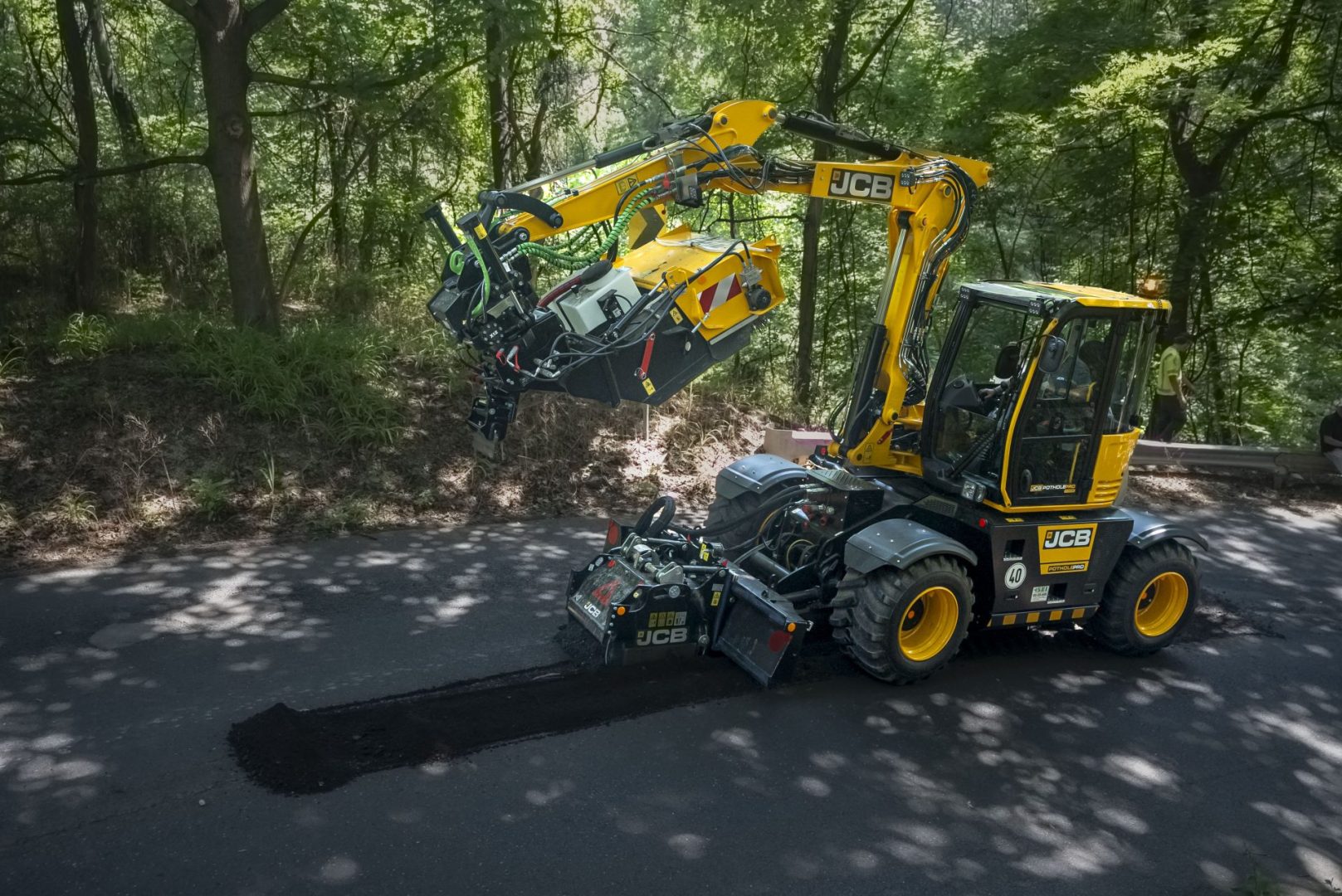 The JCB pothole pro completes a road repair in a treed area
