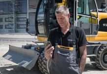 A man looks at the LIebherr MyAssistant app on a smartphone with an excavator in the background